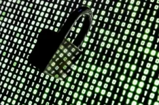 قفل أمام رموز ثنائية (0,1) على شاشة حاسوب محمول، الخلفية سوداء والرموز بلون أخضر فسفوري.